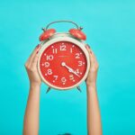 person holding red and beige twin bell analog alarm clock