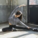 woman in gray long sleeve shirt and black pants sitting on wooden floor