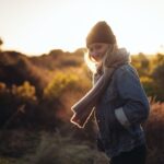 smiling woman taking photo near trees and brown grass during sunrise
